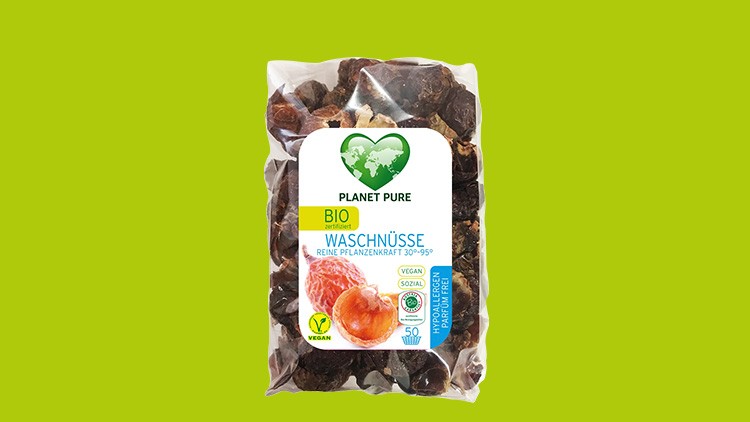 Durchsichtige Verpackung mit braunen Bio-Waschnüssen, Label mit grünem Herz, Schriftzug PLANET PURE und Angaben wie vegan.
