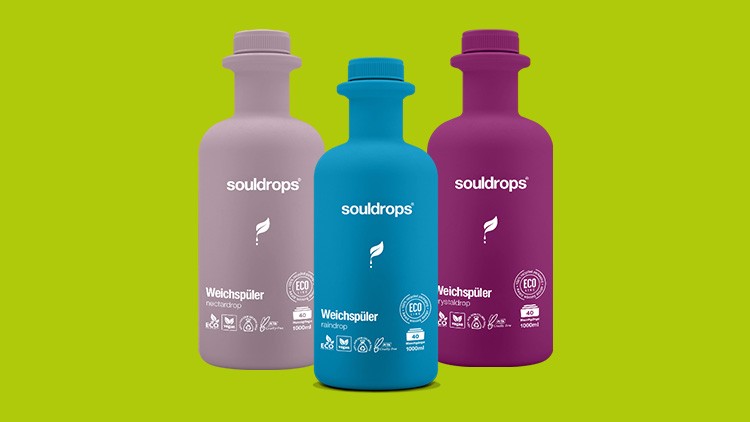 Drei Souldrops-Weichspüler in Flaschen, Farben Lila, Blau und Rosa, mit Eco-Zertifikat und Produktinfos auf grünem Hintergrund.