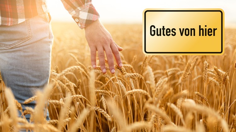 Eine Hand streift Weizenhalme in einem goldenen Feld, daneben ein gelbes Schild mit der Aufschrift Gutes von hier.
