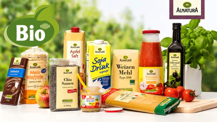 Verschiedene Bio-Lebensmittel von Alnatura, darunter Saft, Mehl, Öl, Tomatenprodukte, Schokolade und frisches Basilikum.
