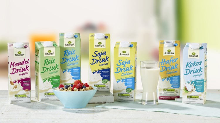 Acht Alnatura-Getränkekartons mit pflanzlichen Drinks stehen neben einer Schale Müsli und einem Glas mit hellem Drink.