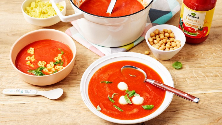 Roter Tomatensuppen-Eintopf mit Basilikum, Mozzarella und weiteren Zutaten wie Nudeln und Kichererbsen auf einem Tisch arrangiert.