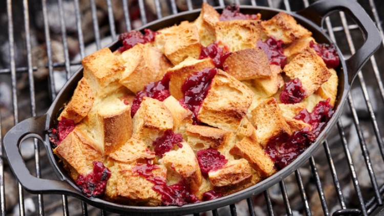 Geröstete Weißbrotwürfel mit roten Beeren und Fruchtsoße in einer ovalen schwarzen Form auf einem Grillrost.