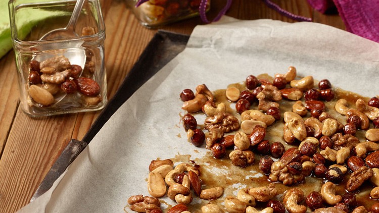 Geröstete Nüsse wie Cashews, Haselnüsse und Walnüsse liegen auf Backpapier, daneben ein Glas mit einem Löffel.