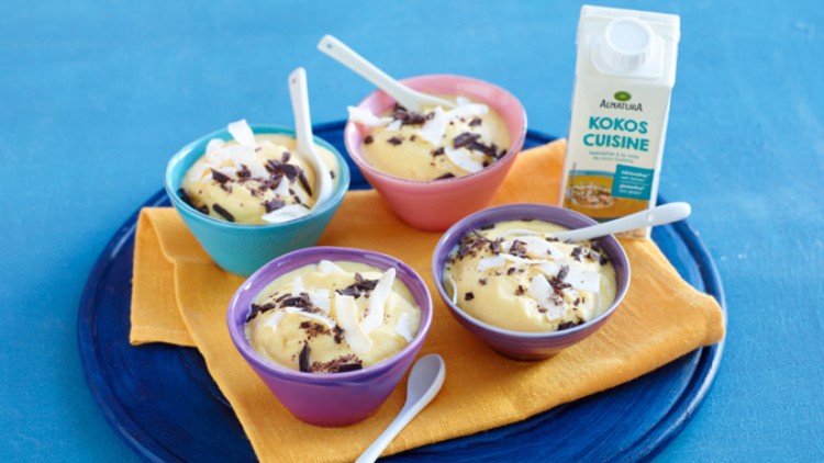 Vier farbige Schalen mit Dessert, garniert mit Kokosraspeln und Schokostückchen, neben einer Alnatura Kokos Cuisine Packung.