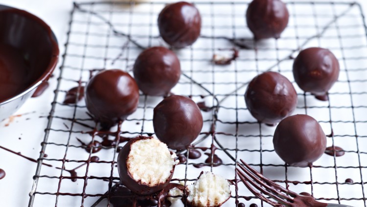 Mehrere Pralinen mit Schokoladenüberzug liegen auf einem Gitter, eine Praline ist angebissen, daneben liegt eine Gabel.
