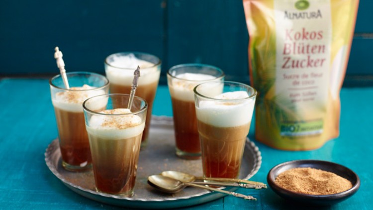 Fünf Gläser Latte Macchiato mit Milchschaum und Dekoration auf Metalltablett, daneben Alnatura Kokosblütenzucker und Schale mit Zucker.