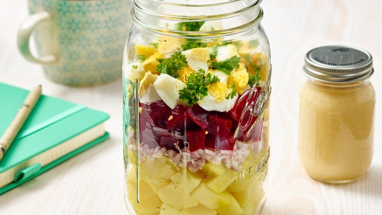 Geschichteter Salat mit Kartoffeln, Roter Bete, Ei und Petersilie in einem Glas, daneben ein Glas mit hellem Dressing.