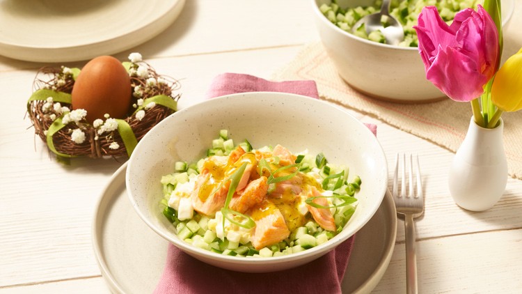 Ein Salat mit Lachs, Gurkenwürfeln und Frühlingszwiebeln auf einem gedeckten Tisch mit Tulpen und einem Osternest.
