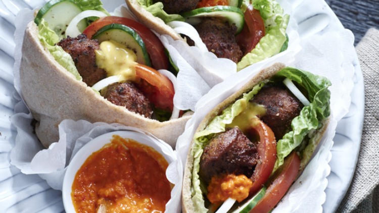 Drei gefüllte Pita-Brote mit Falafel, Salat, Tomaten, Gurken, Zwiebeln und Sauce, serviert mit einem Schälchen roter Soße.