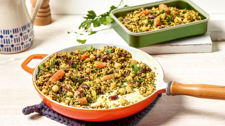 Eine orangefarbene Pfanne mit Quinoa, Kichererbsen, Karotten und Kräutern steht vor einer grünen Auflaufform mit derselben Speise.