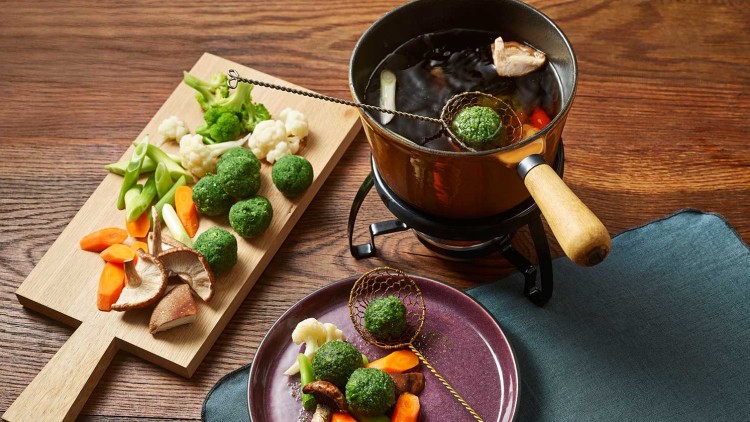 Verschiedene Gemüse wie Karotten, Blumenkohl und Shiitake-Pilze liegen auf Brett und Teller neben einem Fonduetopf.