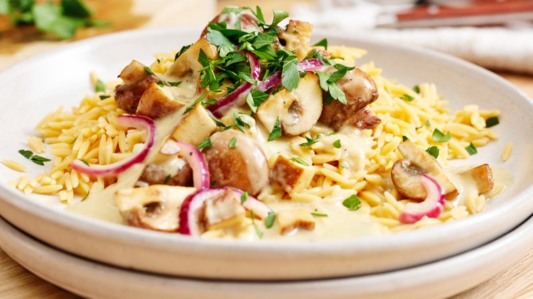 Ein Teller mit gelben Nudeln, geschnittenen Champignons, roten Zwiebeln, cremiger Soße und frischer Petersilie.