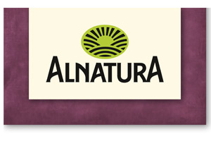 Das Alnatura-Logo mit grünem Halbkreis und schwarzer Schrift auf cremefarbenem Hintergrund, umgeben von einem lila Rand.