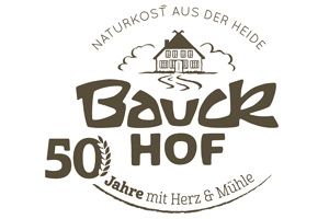 Logo mit Text „Bauck Hof, 50 Jahre mit Herz & Mühle, Naturkost aus der Heide“ und Zeichnung eines Hauses mit Mühlrad.