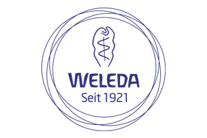 Blaues Logo mit Schriftzug WELEDA Seit 1921, darüber stilisierte Pflanze, umgeben von mehreren dünnen Kreislinien.