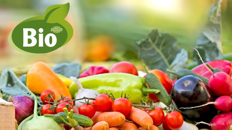 Frisches Bio-Gemüse wie Karotten, Tomaten, Paprika und Radieschen in einer Holzkiste, oben links das Bio-GLOBUS-Logo.