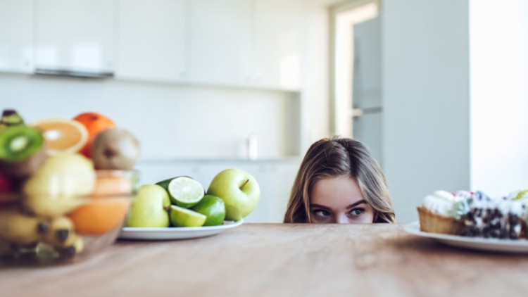 Schale mit Obst, Teller mit grünem Obst und Teller mit Gebäck stehen auf einem Holztisch in einer modernen Küche.