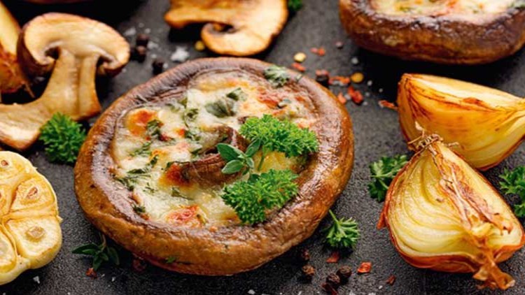 Gefüllte Champignonköpfe mit Käse überbacken, garniert mit frischer Petersilie, neben gebratenen Zwiebeln und Knoblauchhälften.