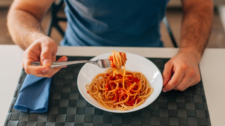 Eine Person sitzt vor einem Teller mit Spaghetti in Tomatensoße und dreht Nudeln mit einer Gabel auf.