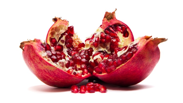 Ein aufgeschnittener Granatapfel mit roten Kernen auf weißem Hintergrund, einige Kerne liegen davor.