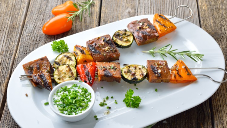 Zwei Grillspieße mit Gemüse und Fleisch auf weißem Teller, garniert mit Kräutern und Schälchen mit grünem Dip.