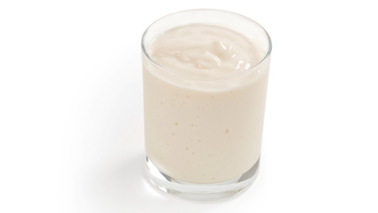 Ein durchsichtiges Glas ist mit cremigem, hellbeigem Joghurt oder Dessert gefüllt.