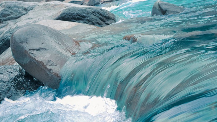 Klares Wasser eines Flusses strömt über glattgeschliffene graue Steine in einer natürlichen Umgebung.