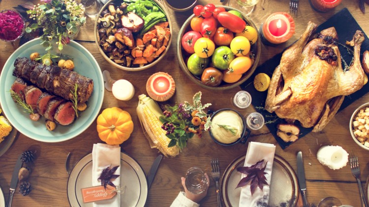 Ein gedeckter Tisch mit Dekoration wie Kürbissen und Kerzen sowie Speisen wie Gemüse, Truthahn, Maiskolben und Salat.