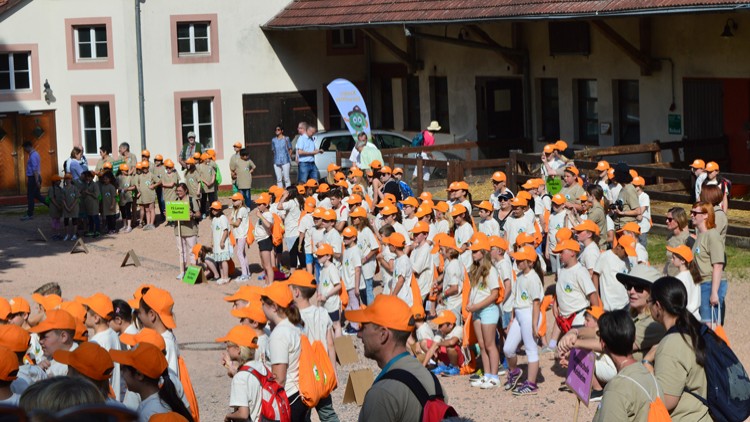 Viele Menschen in weißen und grünen T-Shirts sowie orangen Basecaps stehen auf einem Hof vor Gebäuden und einem Globini-Banner.