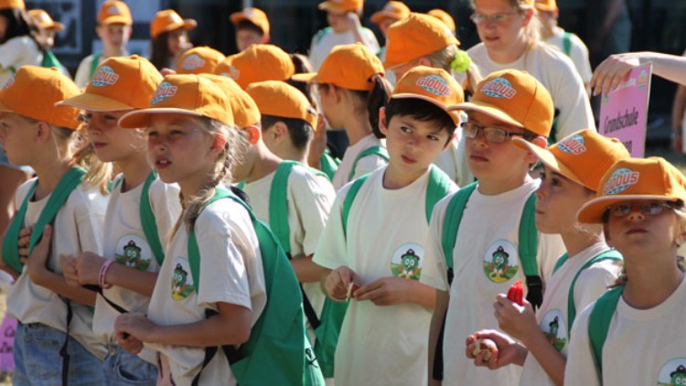 Menschen in weißen T-Shirts mit Globini-Logo und orangefarbenen GLOBUS-Kappen stehen in einer Gruppe im Freien.