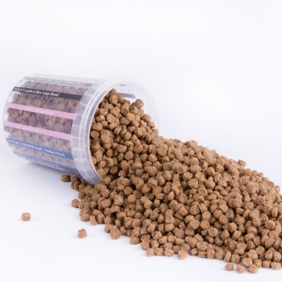 Ein transparenter Behälter liegt auf der Seite, Trockenfutter für Hunde in braunen Pellets fällt auf eine weiße Unterlage.