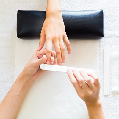 Eine Hand wird auf einem schwarzen Kissen abgelegt, während eine andere Hand eine Nagelfeile an einem Fingernagel anwendet.