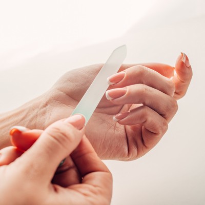 Eine Hand feilt mit einer transparenten Glasnagelfeile die Fingernägel der anderen Hand in heller Umgebung.