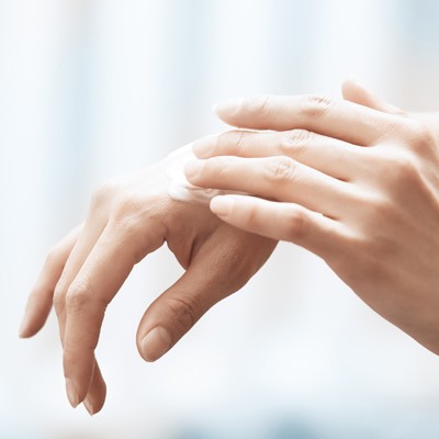 Eine Hand trägt weiße Creme auf den Handrücken einer anderen Hand auf, Hintergrund unscharf in hellen Tönen.