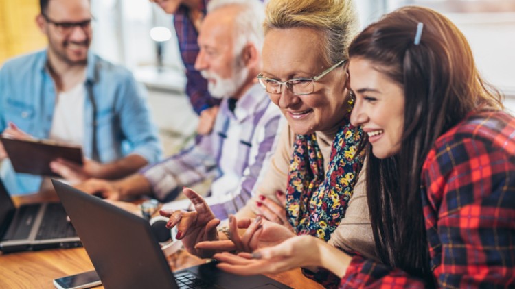 Personen sitzen an einem Tisch mit Laptops und Tablets und diskutieren in einer Arbeits- oder Lerngruppe.