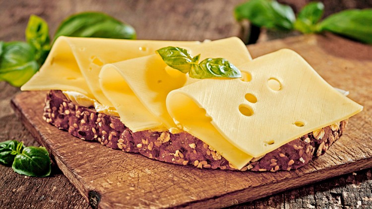 Ein mit Käse belegtes Vollkornbrot liegt auf einem Holzbrett, dekoriert mit frischen Basilikumblättern.