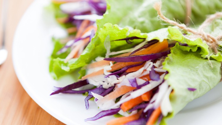 Zwei Salatblatt-Wraps gefüllt mit Streifen von Rotkohl, Karotten und anderem Gemüse auf einem weißen Teller.