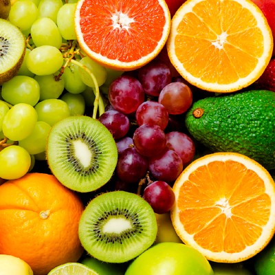 Aufgeschnittene Orangen und Kiwis liegen mit ganzen grünen und roten Trauben, einer Avocado, Äpfeln und einer Orange zusammen.