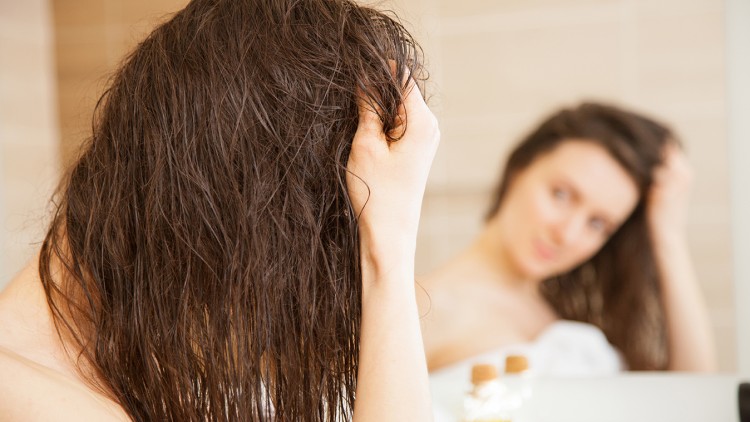Person mit nassen, braunen Haaren hält sich den Kopf, im Vordergrund Fläschchen mit gelber Flüssigkeit und unscharfer Spiegelhintergrund.
