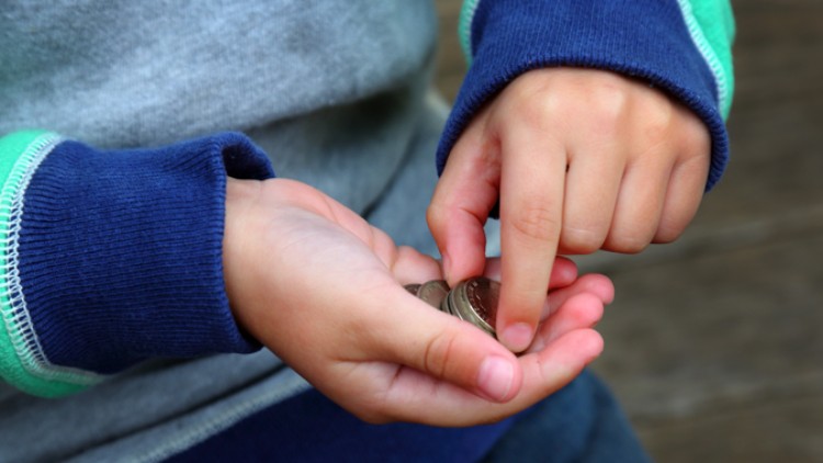 Zwei Kinderhände halten mehrere Münzen, wobei eine Hand mit dem Zeigefinger auf eine Münze zeigt.