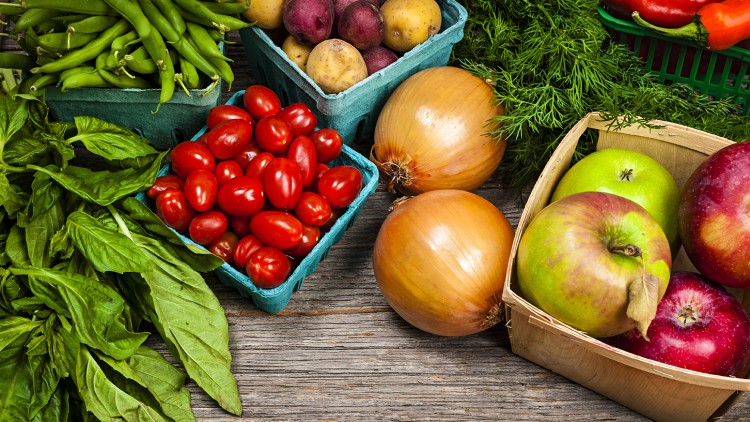 Frisches Obst, Gemüse und Kräuter wie Äpfel, Zwiebeln, Tomaten, Kartoffeln, grüne Bohnen, Basilikum und Dill auf Holztisch.