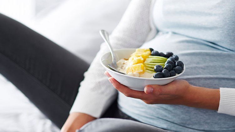 Eine Person hält eine Schüssel mit Haferbrei, geschnittenem Obst wie Kiwi, Ananas und Blaubeeren sowie einem Löffel in der Hand.