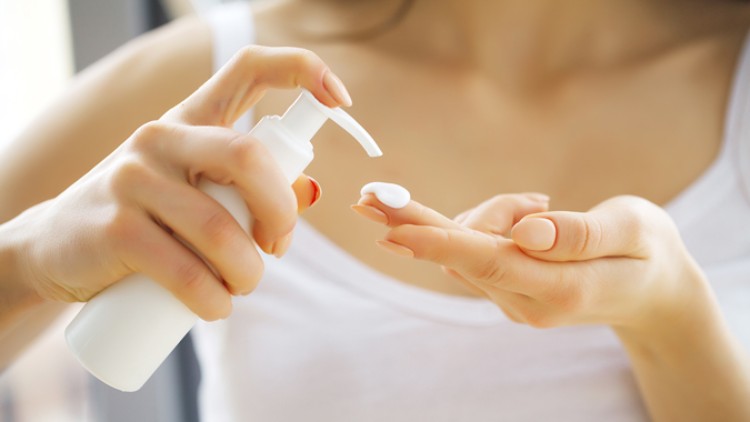 Eine Person in weißem Oberteil drückt weiße Creme aus einem Spender auf die Fingerspitzen der anderen Hand.