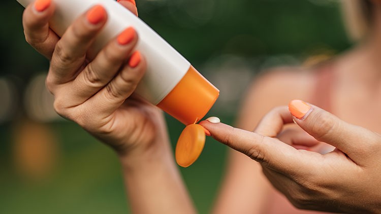 Eine orange-weiße Tube wird gedrückt, und eine kleine Menge Creme wird auf einen Finger aufgetragen, Hände mit orangen Nägeln.