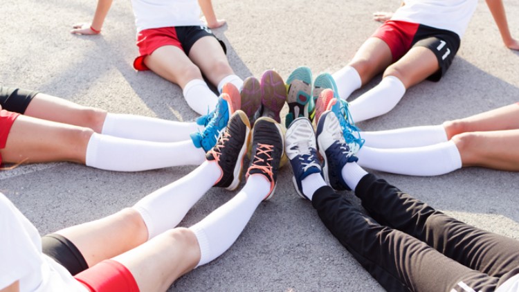 Menschen sitzen im Kreis auf dem Boden, ihre Füße in Sportschuhen und weißen Kniestrümpfen berühren sich in der Mitte.