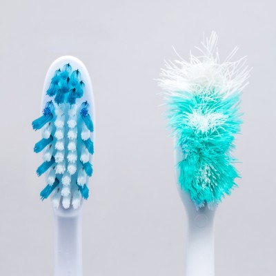 Eine neue Zahnbürste mit blauen und weißen Borsten neben einer abgenutzten Zahnbürste mit ausgefransten Borsten.