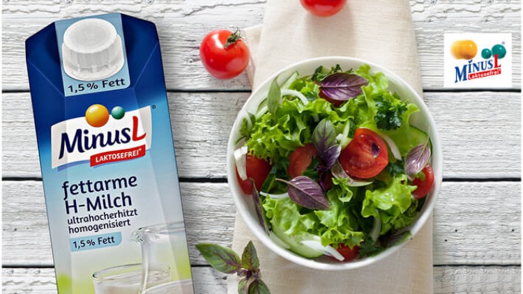 Eine Packung MinusL fettarme H-Milch mit 1,5 % Fett steht neben einem frischen Salat mit Tomaten und Basilikum auf Holzuntergrund.