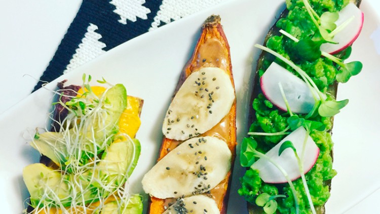 Drei Süßkartoffelhälften mit Avocado, Sprossen, Bananenscheiben, Chiasamen, Erdnussbutter, Erbsenpüree und Radieschen auf Teller.