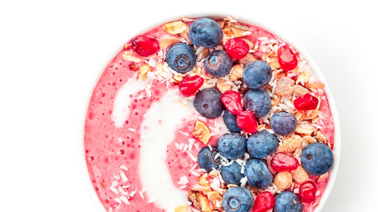Schale mit rotem Smoothie, dekoriert mit Blaubeeren, Granatapfelkernen, Müslistückchen, Kokosraspeln und weißem Joghurt.